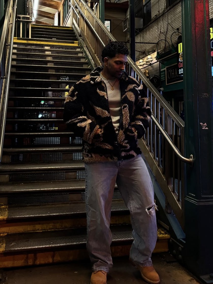Jason in a patterned fleece jacket and light jeans on the stairs of a NYC elevated subway station